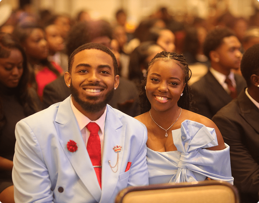 Smiling couple dressed formally at an event with a warm ambiance.