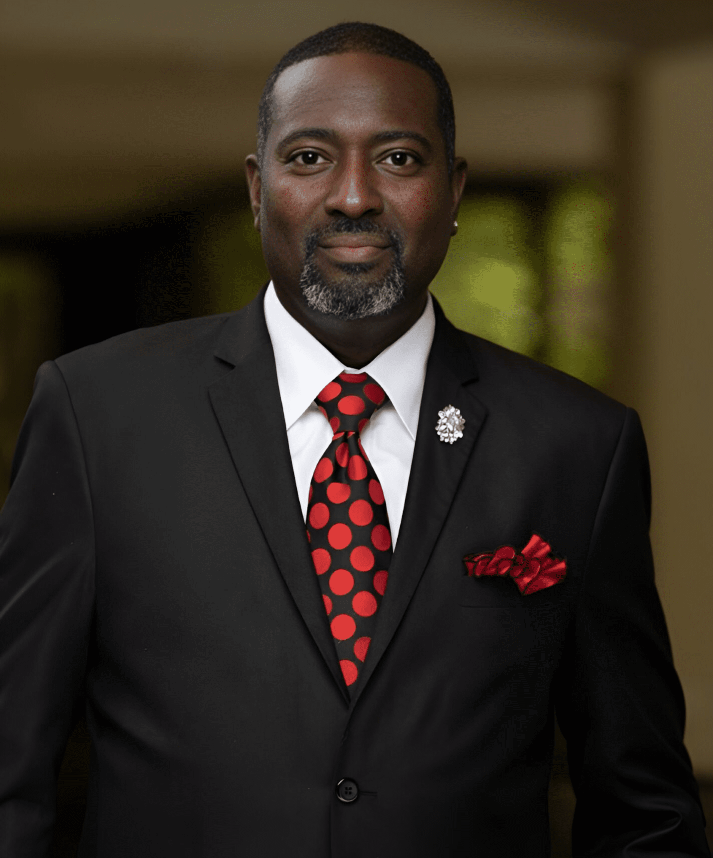 Man in a black suit with a red polka dot tie and matching pocket square.